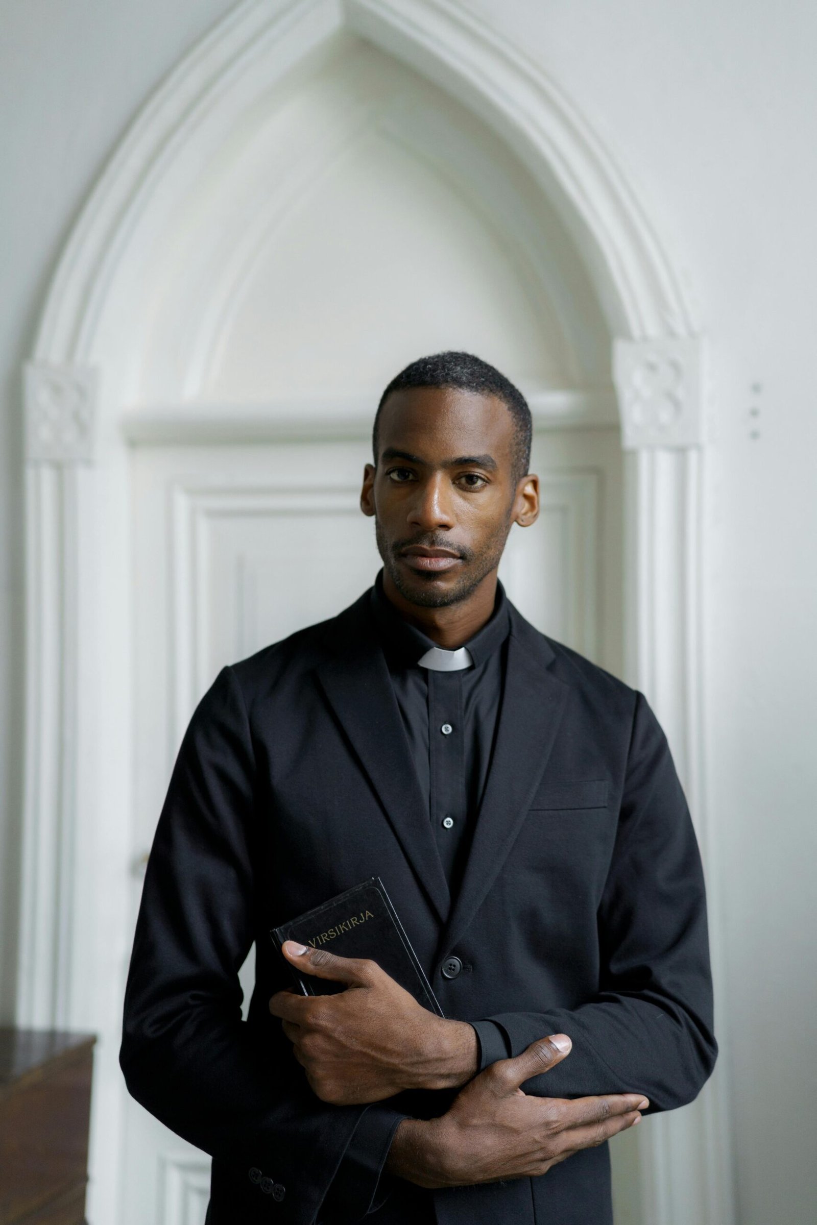 Stylish pastor in a church setting holding a book, contemplating faith and spirituality.